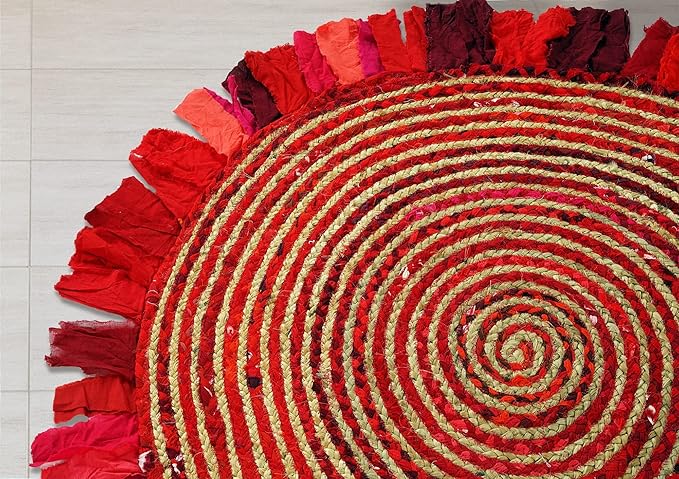Round red and gold braided rug with fringes on a light wooden floor.