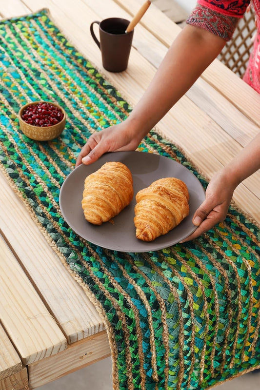Person holding a plate with two croissants on a colorful woven mat.