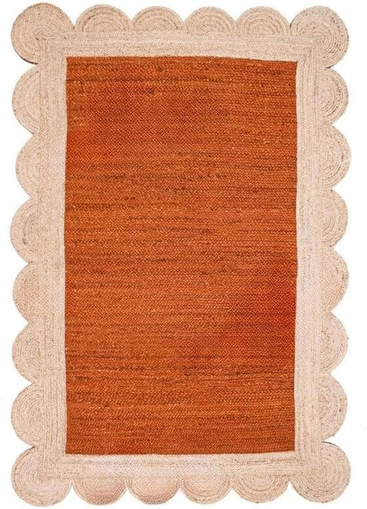 A rectangular woven rug with a warm rust-orange center and a natural beige scalloped braided border, shown flat against a white background.