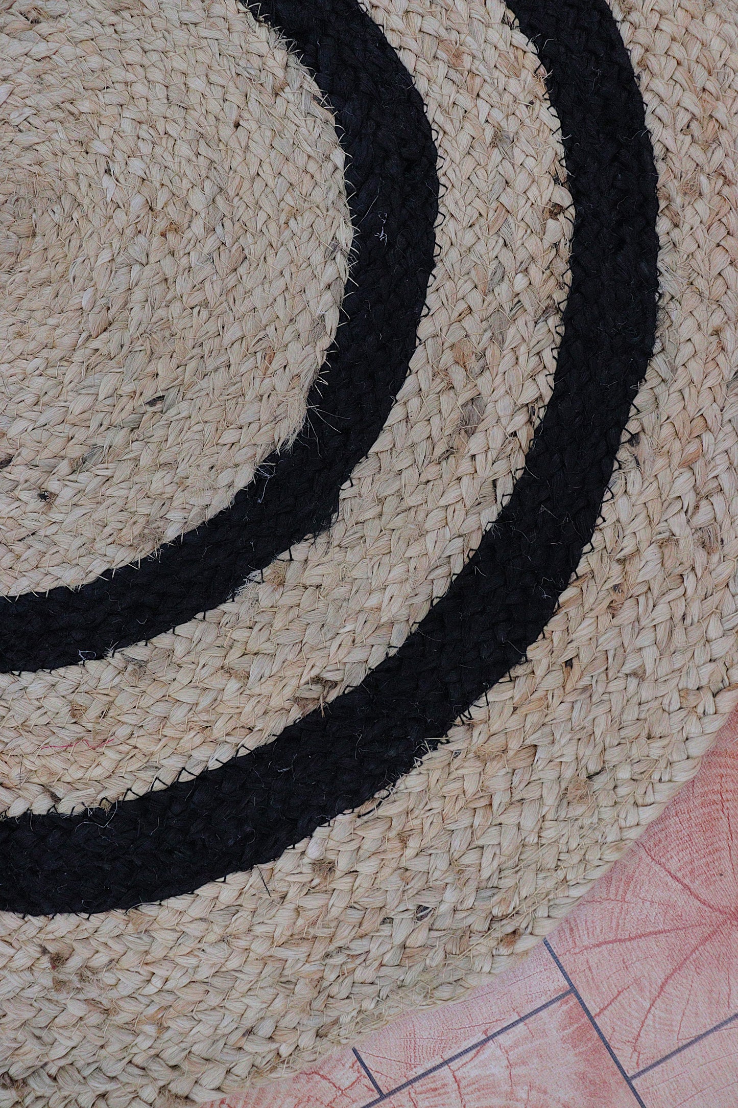 Close-up of a woven mat with black circular pattern on a textured surface.