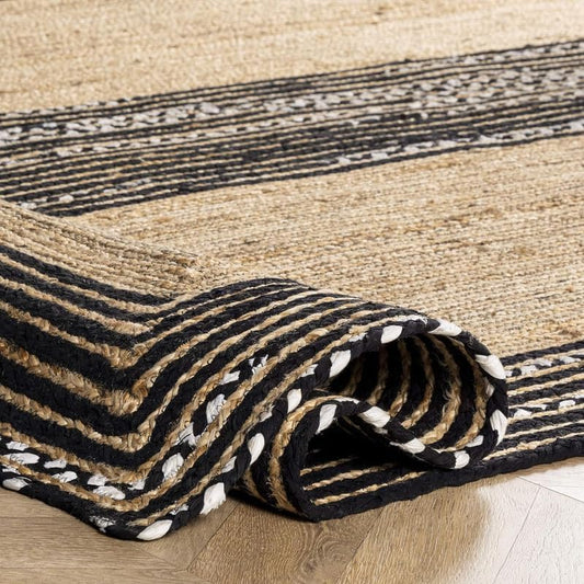 Rolled-up striped rug with black, beige, and white pattern on a wooden floor.