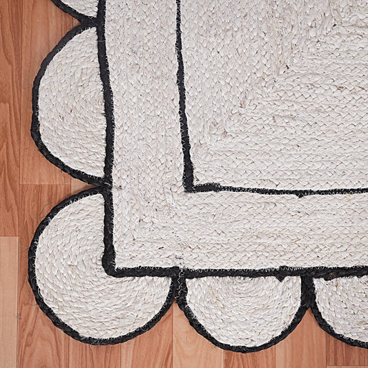 White braided rug with black scalloped edge on a wooden floor