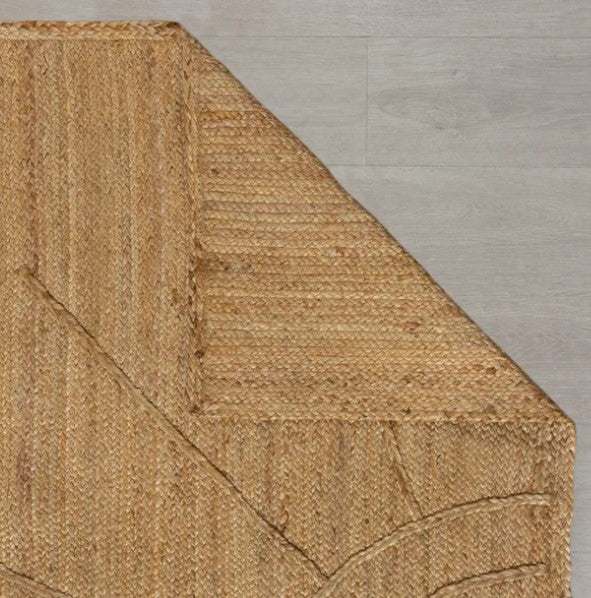 Close-up of a woven natural fiber rug corner on a wooden floor.