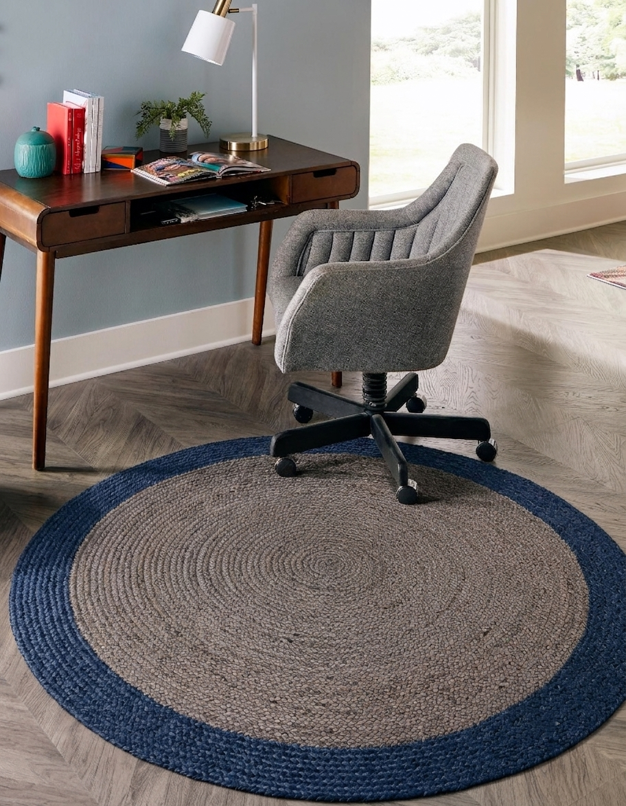 Blue and natural jute round rug with solid center and border pattern under a desk chair in a living room floor carpet