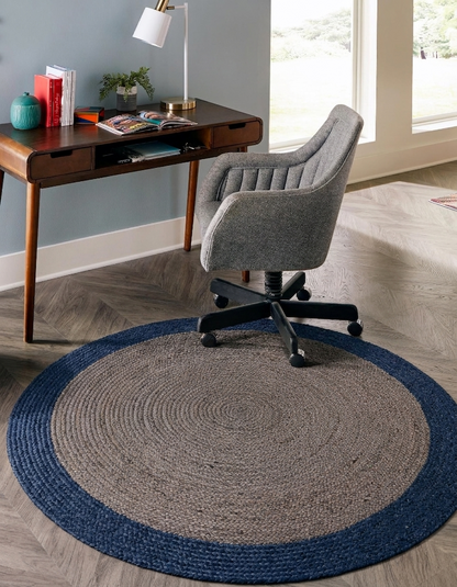 Blue and natural jute round rug with solid center and border pattern under a desk chair in a living room floor carpet