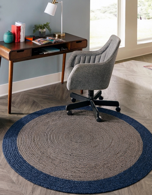 Blue and natural jute round rug with solid center and border pattern under a desk chair in a living room floor carpet