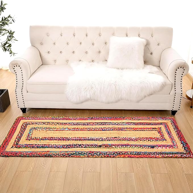 Colorful braided rug on a wooden floor in front of a white tufted sofa.