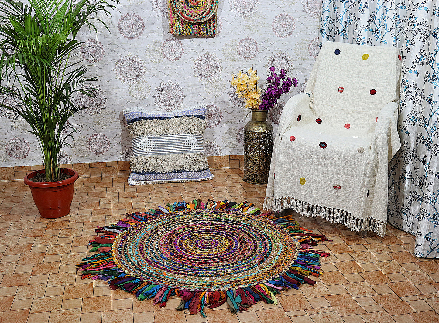 Colorful round rug with tassels in a room with a chair, plant, and wall decor.