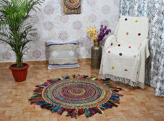 Colorful round rug with tassels in a room with a chair, plant, and wall decor.