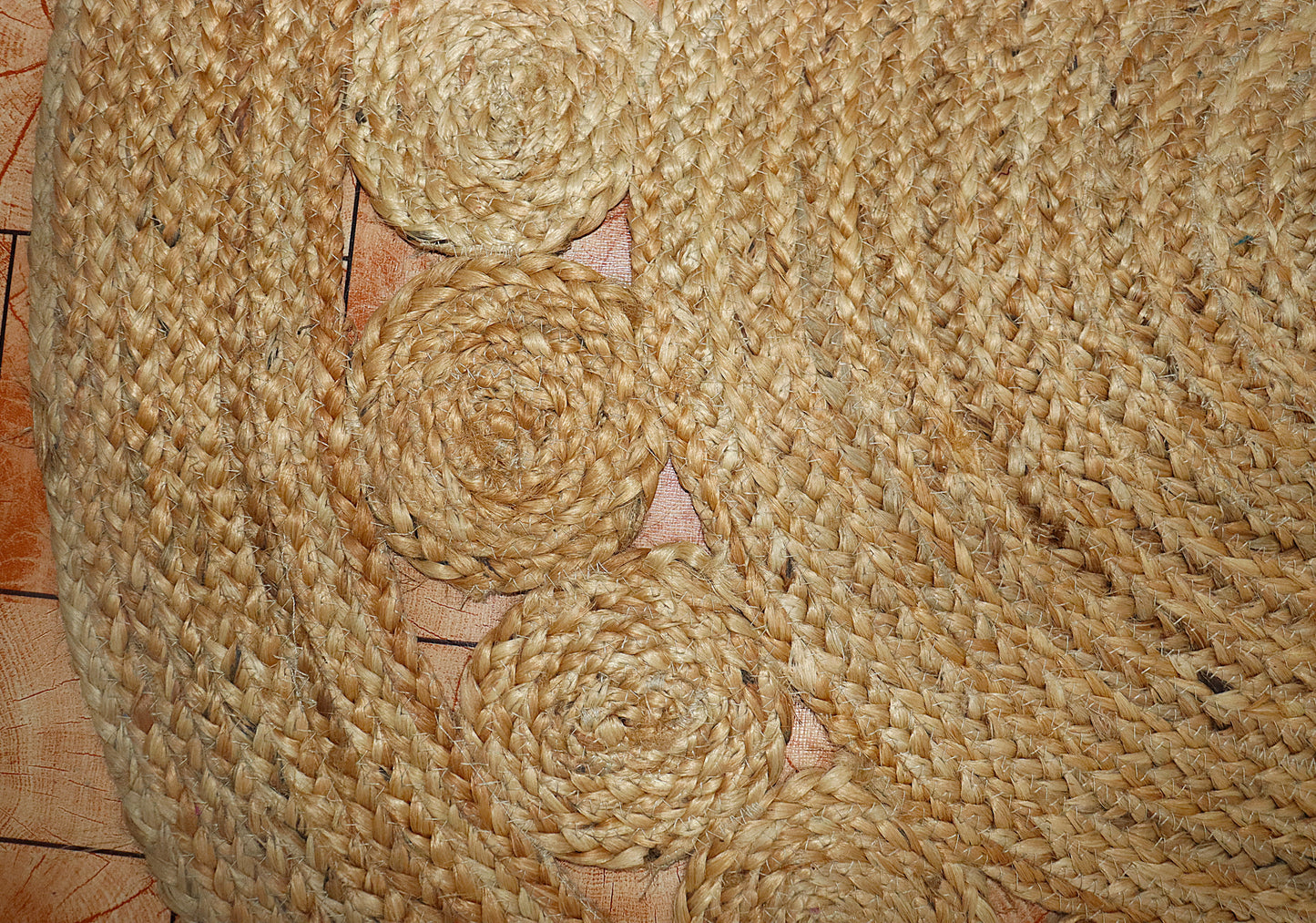 Close-up of a woven jute mat with spiral patterns on a wooden surface.