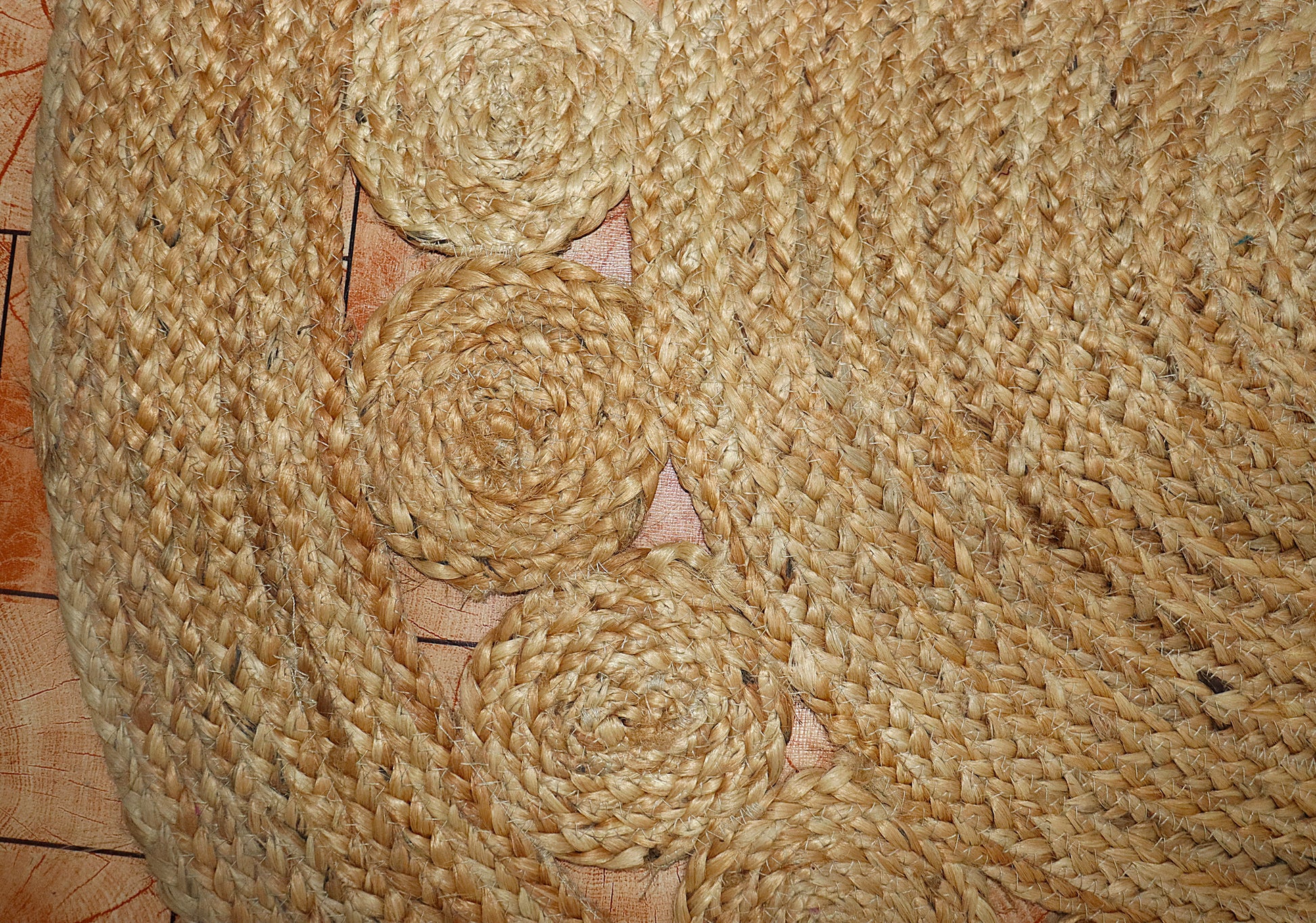 Close-up of a woven jute mat with spiral patterns on a wooden surface.