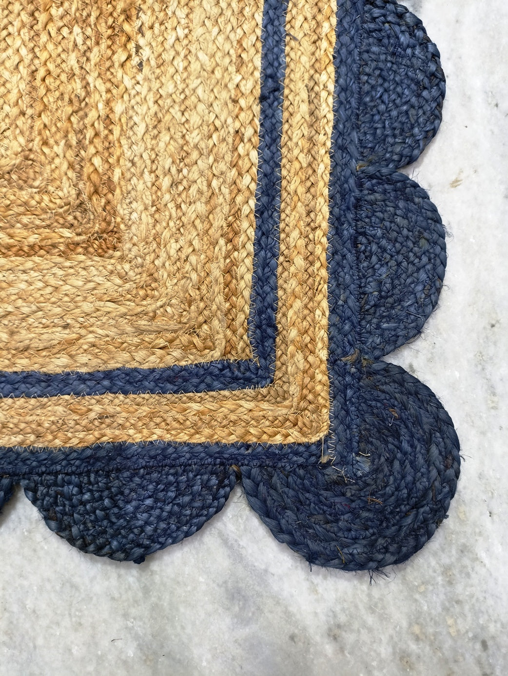 Close-up of a jute rug with blue scalloped edge on a light background