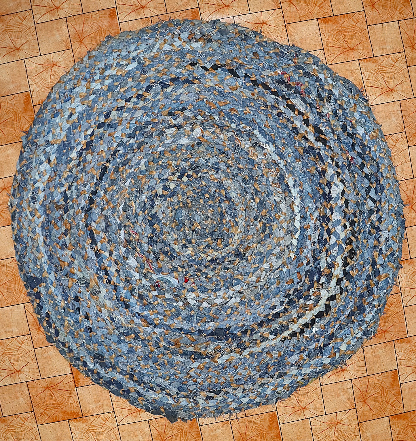 Round braided rug made from recycled denim on a wooden floor.