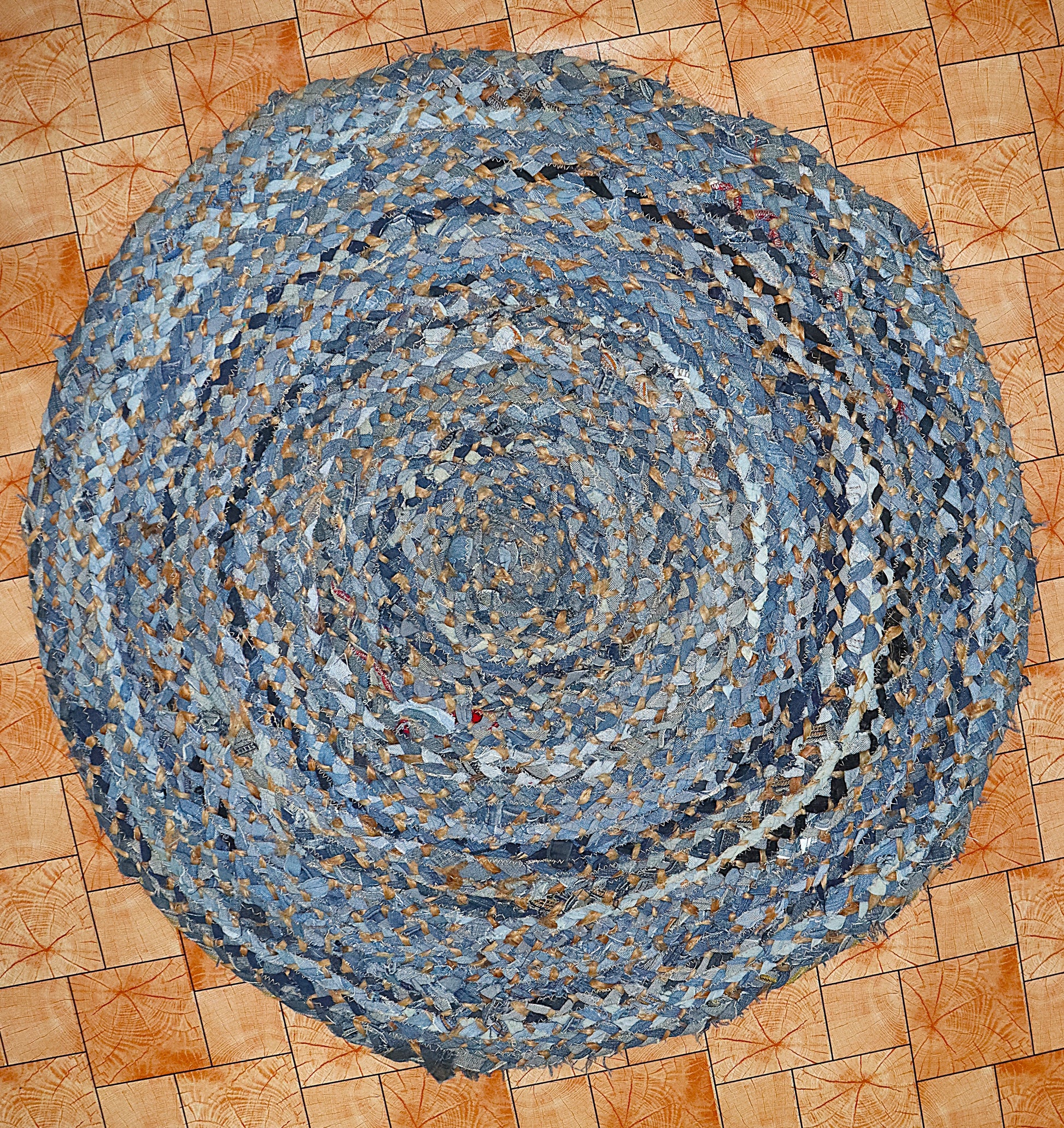 Round braided rug made from recycled denim on a wooden floor.