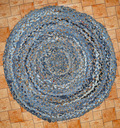 Round braided rug made from recycled denim on a wooden floor.
