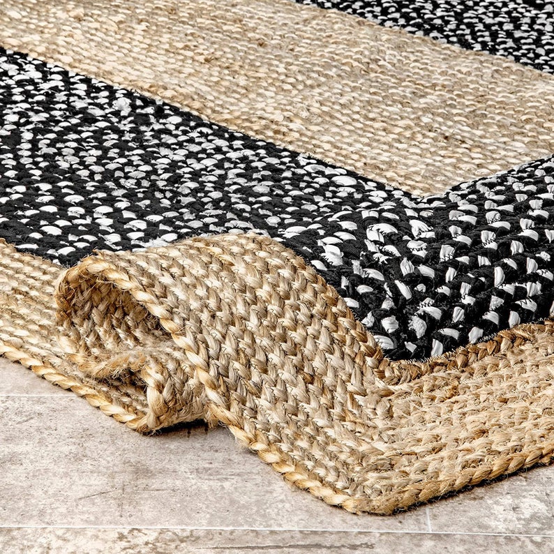 Close-up of a woven jute and black and white patterned rug on a wooden floor.