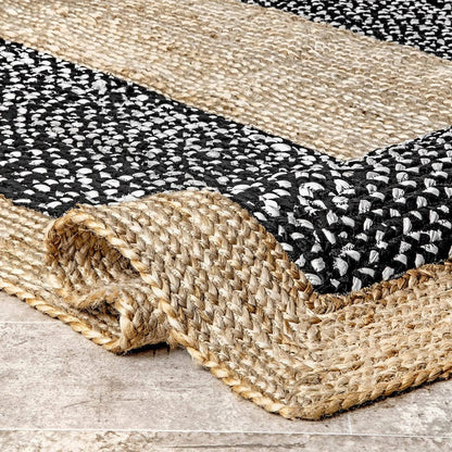 Close-up of a woven jute and black and white patterned rug on a wooden floor.