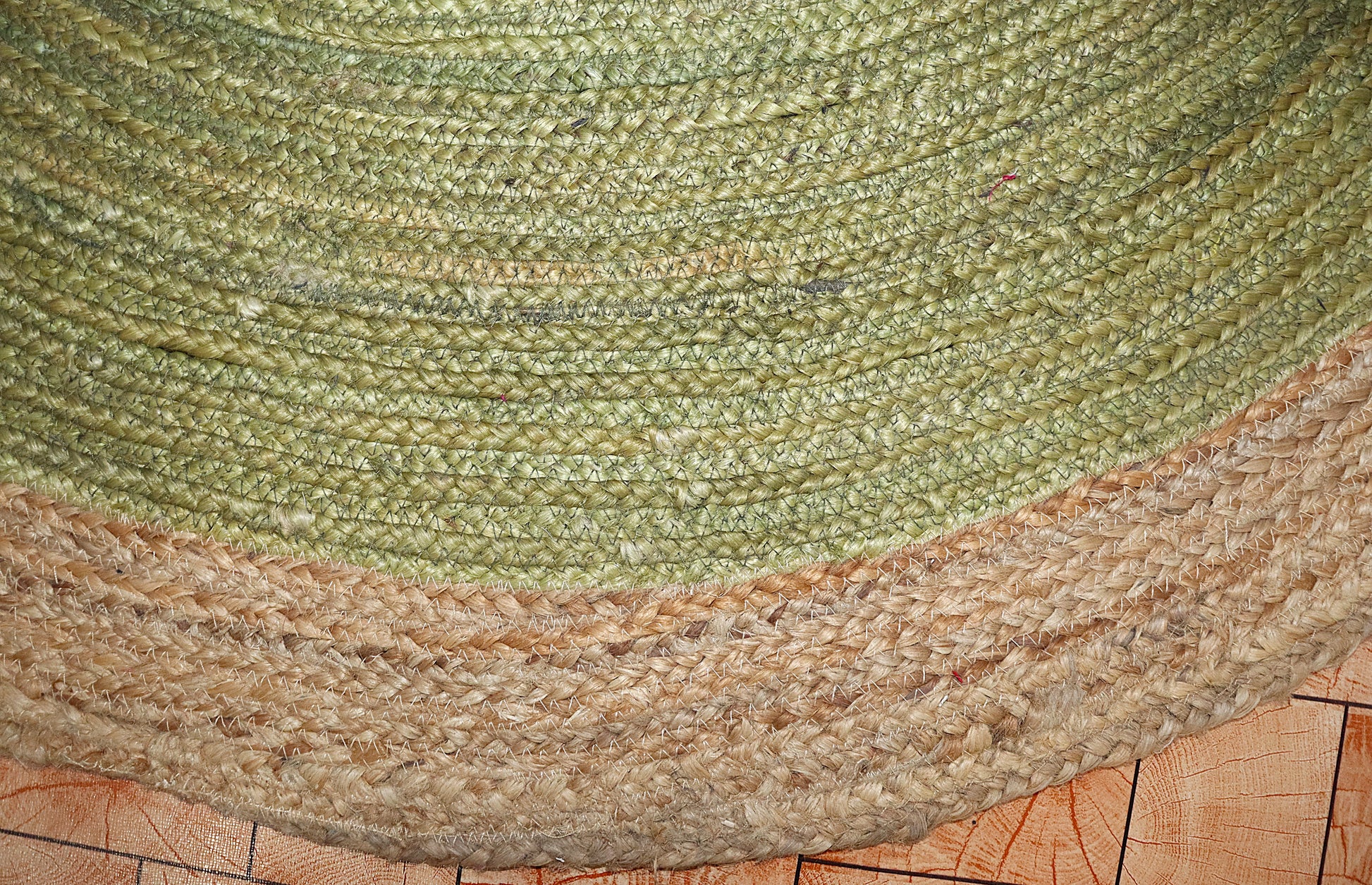 Close-up of a green and beige braided rug on a wooden floor.