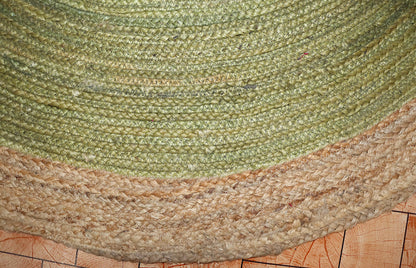 Close-up of a green and beige braided rug on a wooden floor.