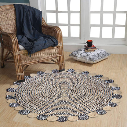 Round braided rug with black and white pattern on a wooden floor, accompanied by a wicker chair and cushion.