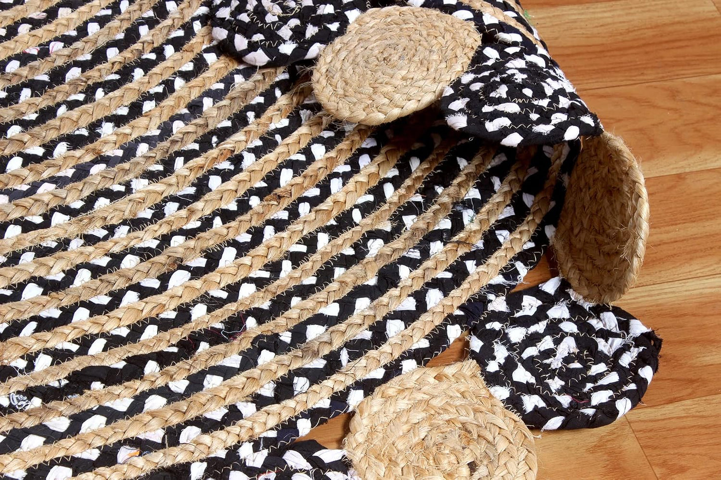 A braided jute rug with a black and white patterned top and three round natural jute cowhide-style pads attached, shown on a light wood floor.