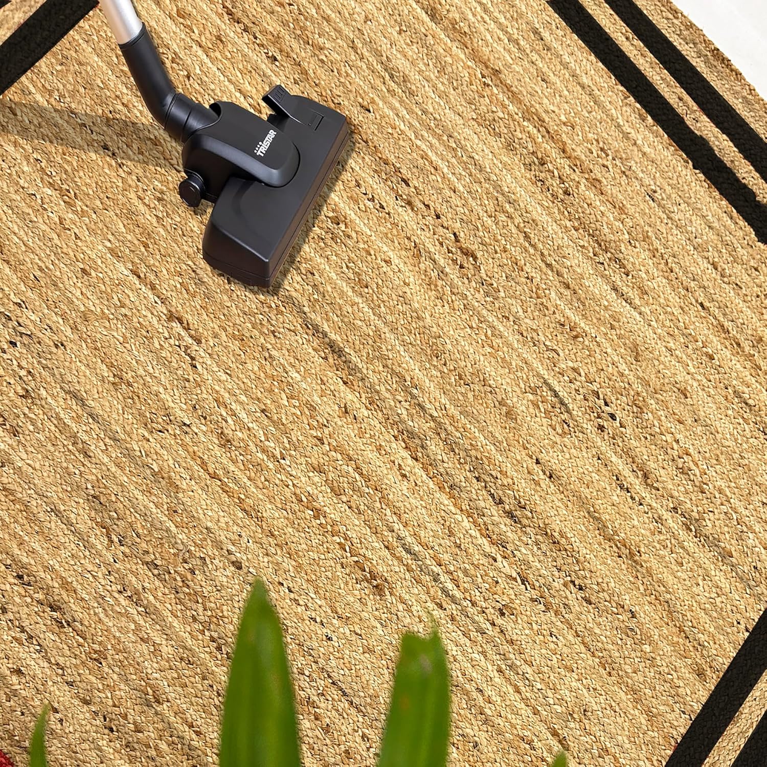 Natural Jute Area Rug with black border being vacuumed, ideal for living room or entryway use.