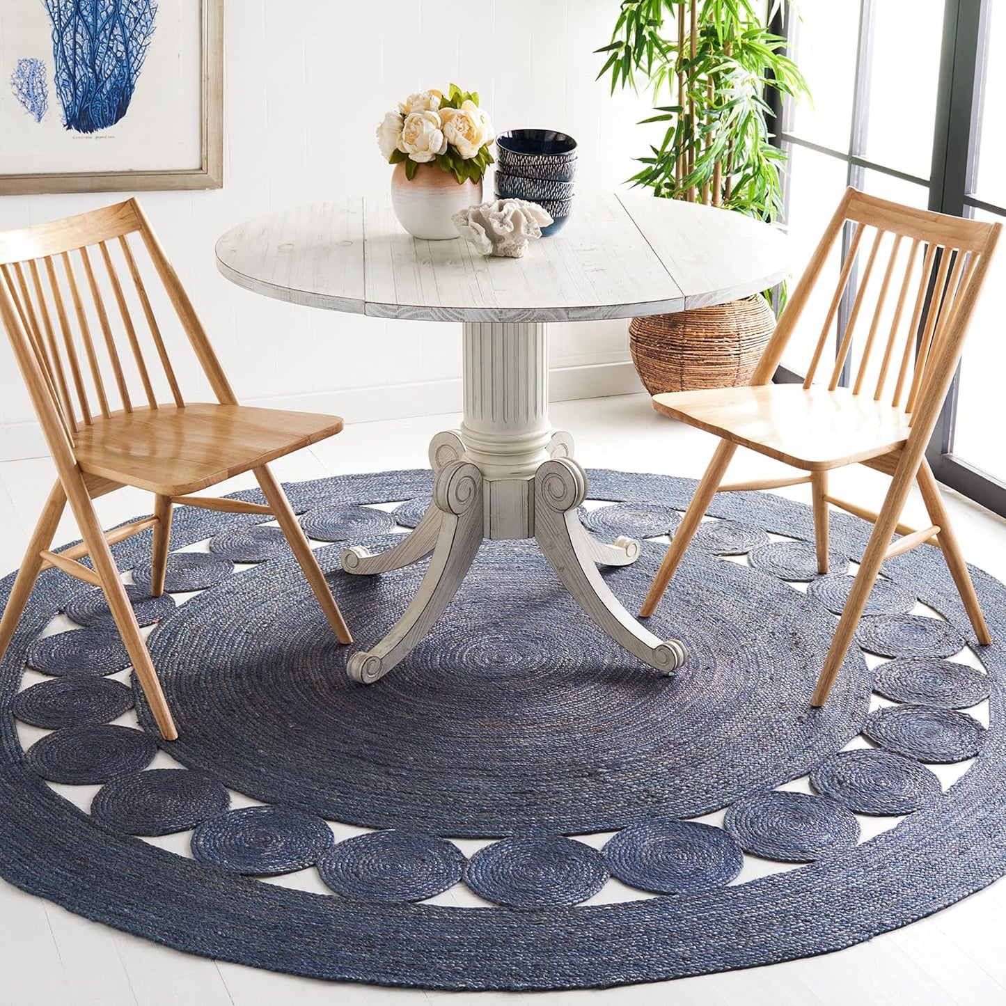 Stylish round blue braided area rug under a white dining table with wooden chairs and decor.