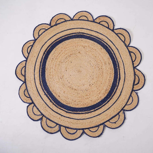 A round woven jute placemat with a scalloped outer border and concentric navy blue stripes, laid flat on a light off-white background.
