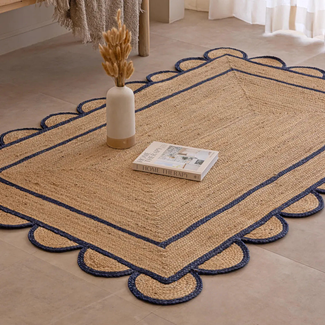 Nautical-style rug with scalloped edge on a wooden floor, featuring a vase and book.