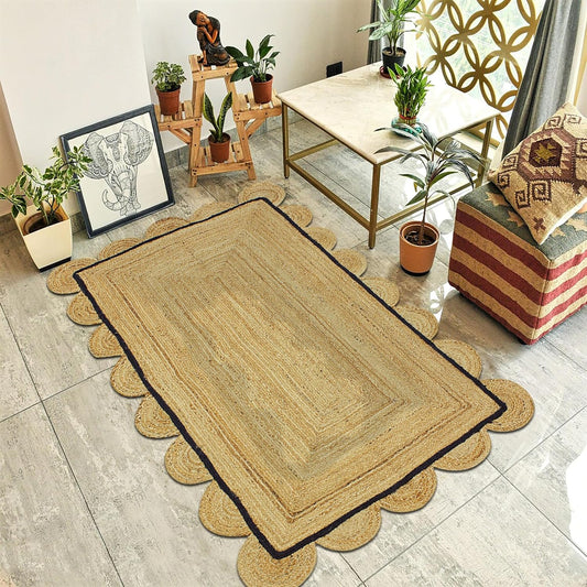 A rectangular natural jute area rug with scalloped edges and a dark border, styled in a modern living room setting on a light gray tiled floor.
