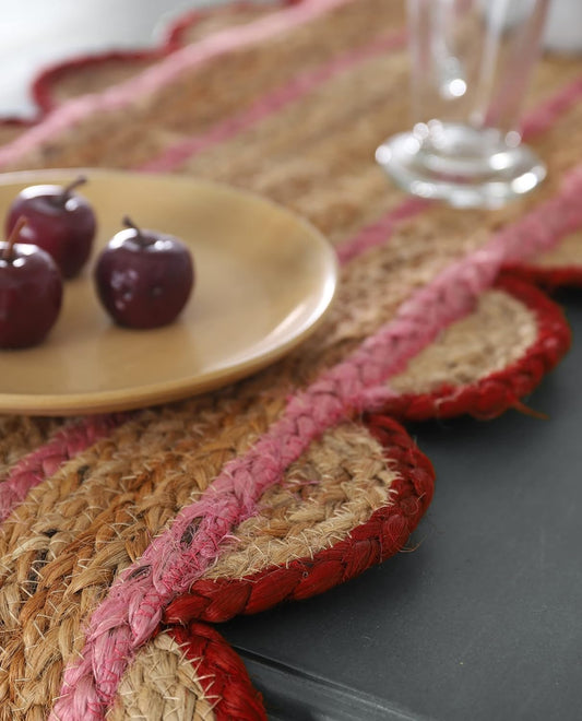 Placemats with red trim on a table with a plate of cherries and a glass.