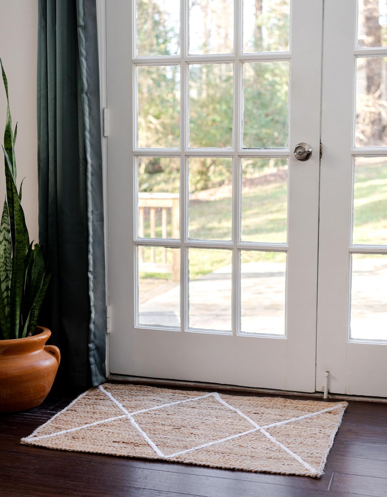 Doormat with geometric pattern in front of a glass door leading to a garden.