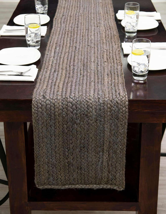 Knitted table runner on a wooden dining table with plates and glasses.
