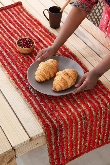 Person holding a plate of croissants on a red and brown striped table runner.