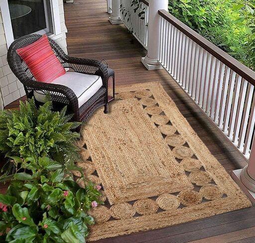 Wicker chair with red and white cushions on a wooden deck with a decorative jute rug.