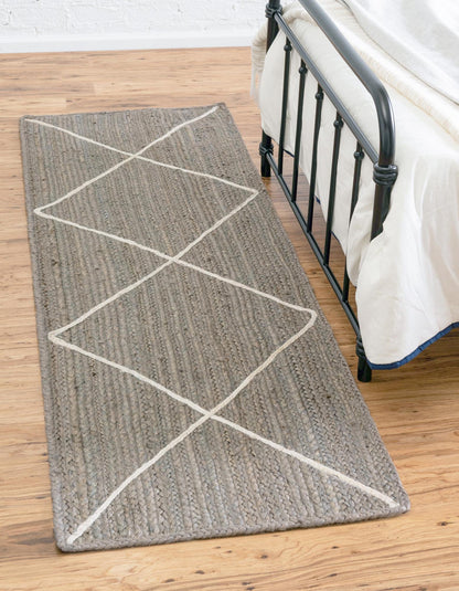 Gray rug with white geometric pattern on a wooden floor next to a bed.