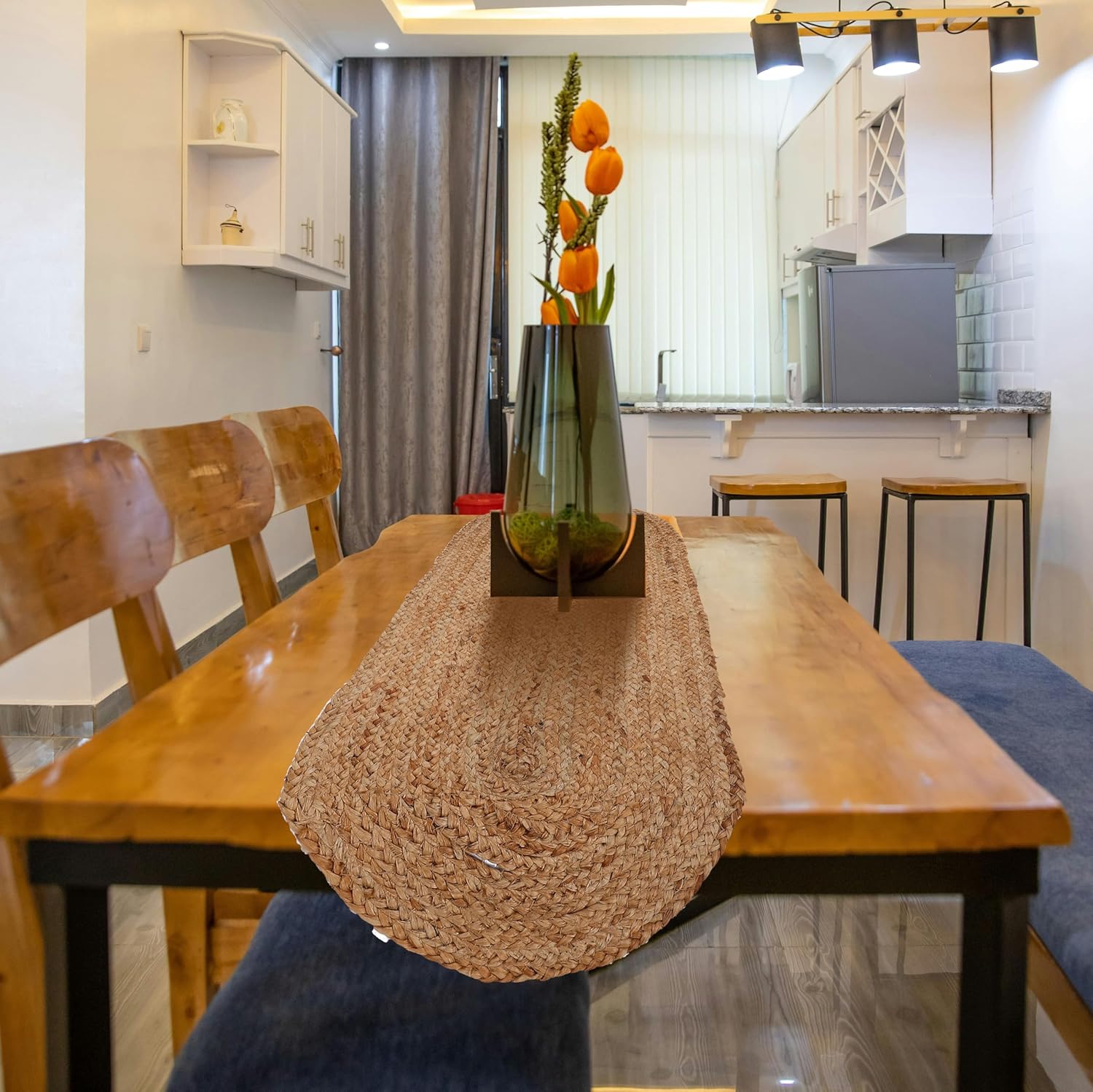 Dining table with a woven runner and a vase of flowers in a kitchen setting