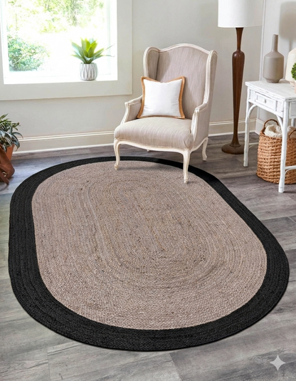 Oval-shaped rug with black border on a wooden floor in a room with a chair and decor.