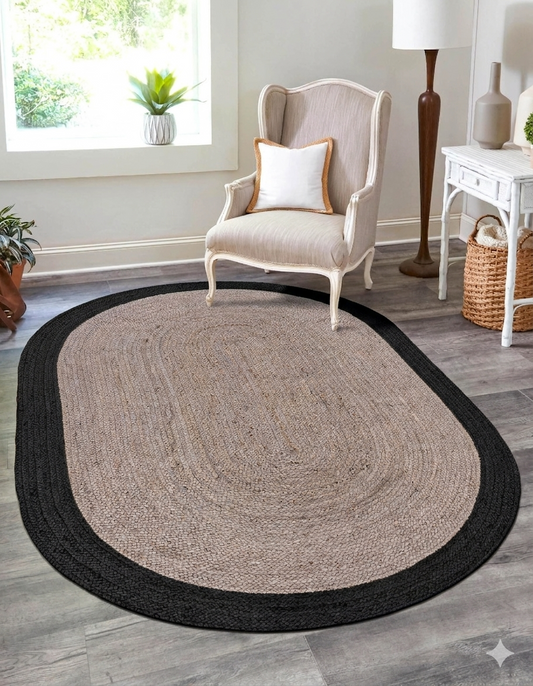 Oval-shaped rug with black border on a wooden floor in a room with a chair and decor.