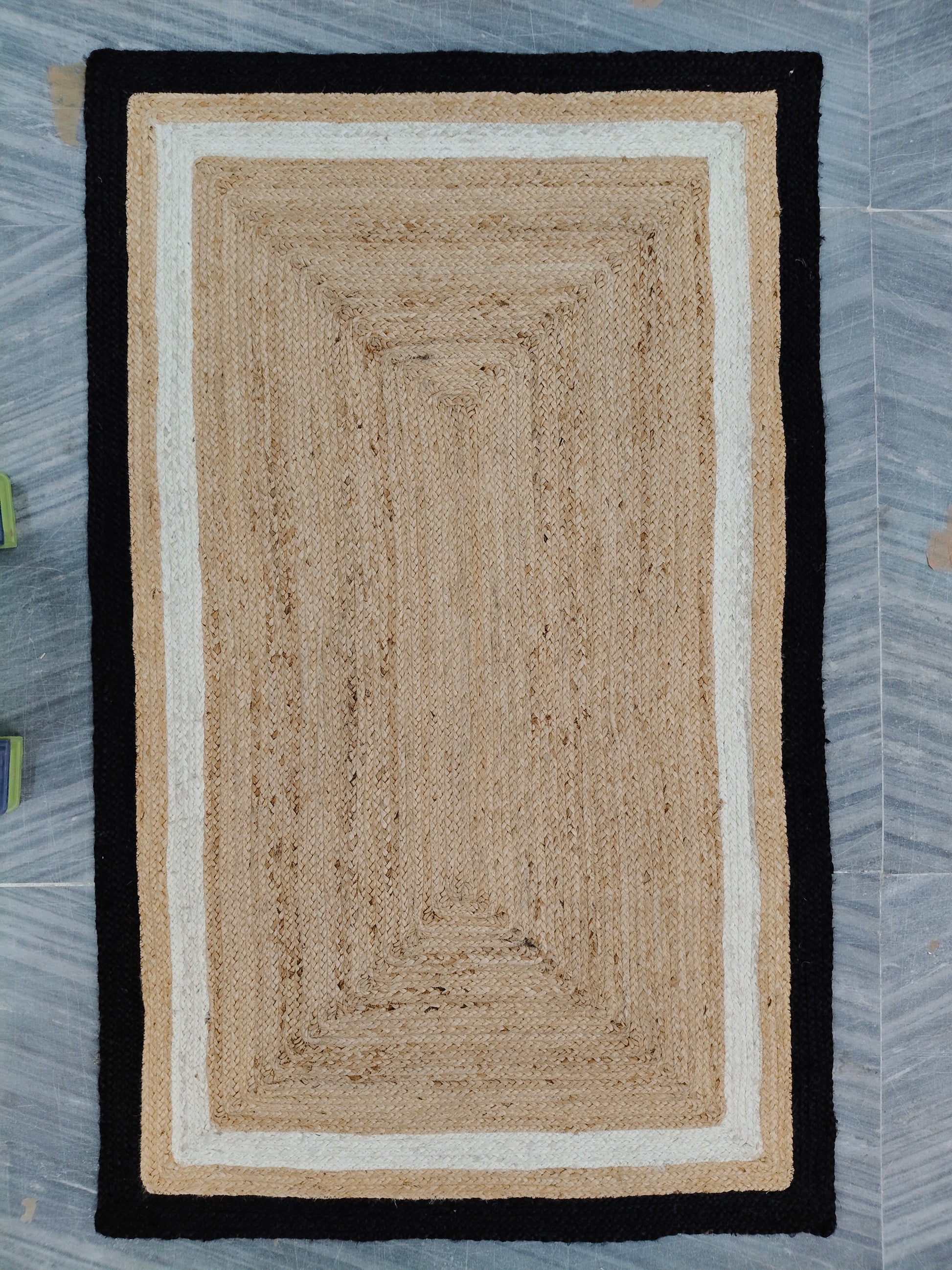 Rectangular braided rug with black border on a gray floor