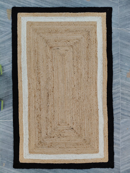 Rectangular braided rug with black border on a gray floor