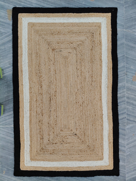 Rectangular braided rug with black border on a gray floor