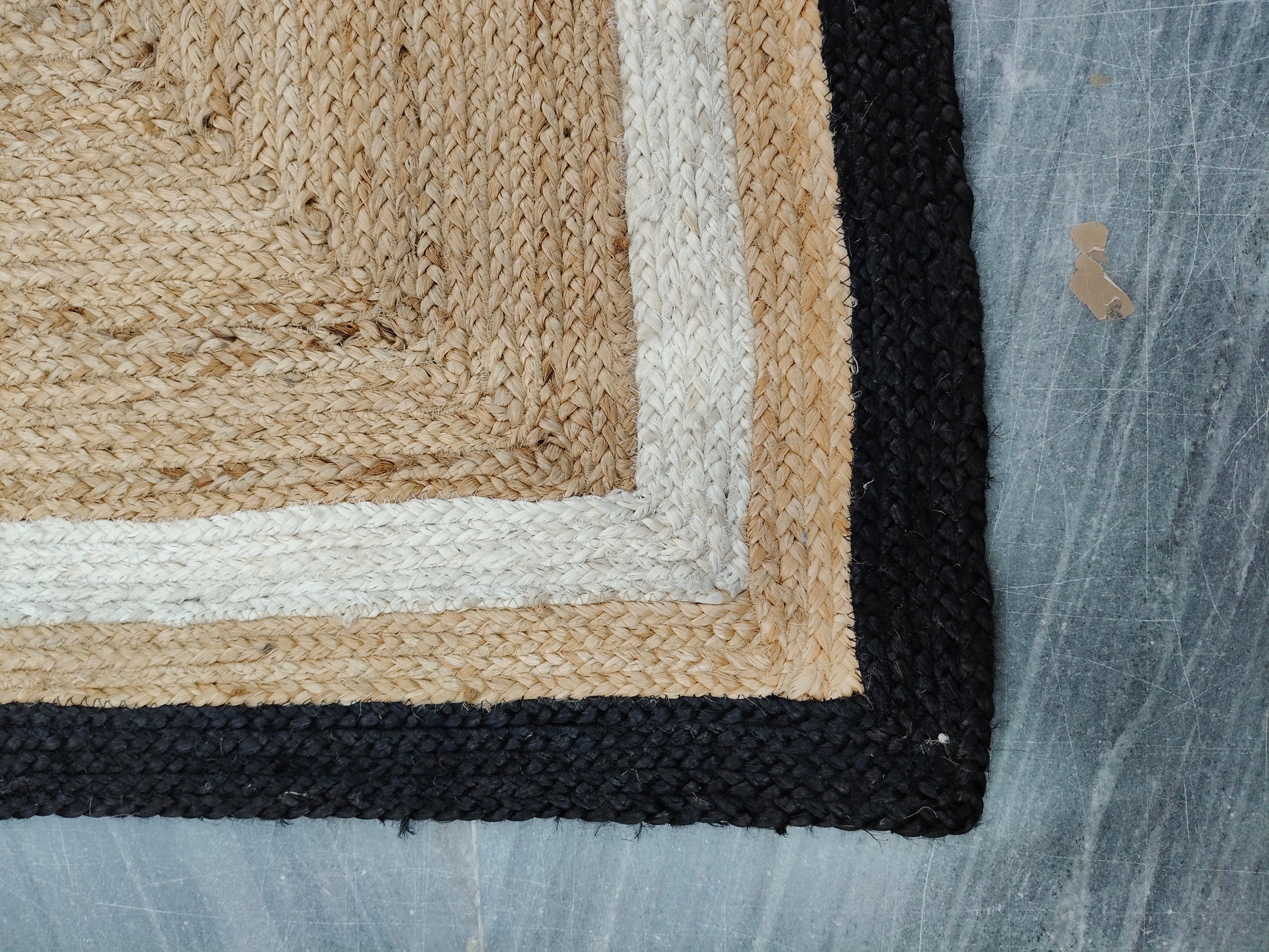 Close-up of a textured rug corner with beige, black, and white border on a blue fabric background.
