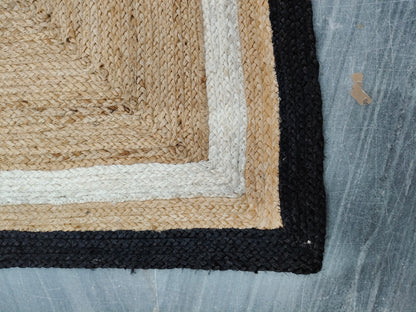 Close-up of a textured rug corner with beige, black, and white border on a blue fabric background.