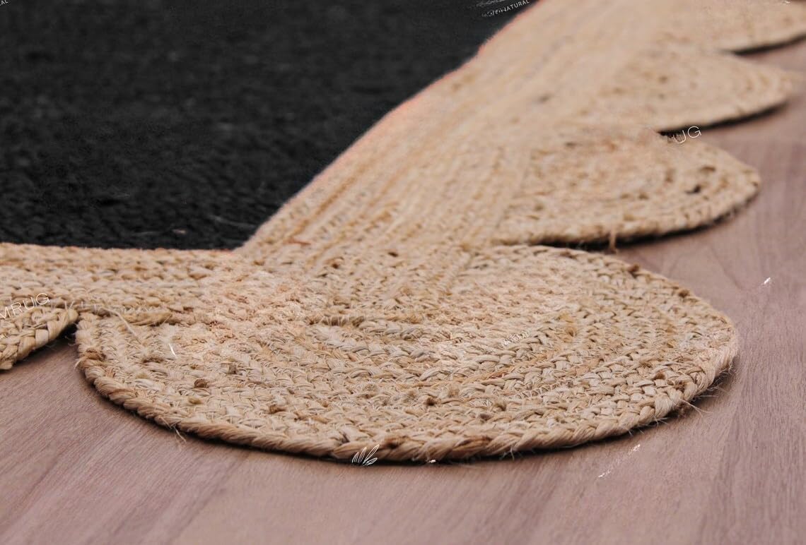 A close-up of a natural jute or sisal rug with a scalloped edge, laid over a black rug on a light brown wooden floor.