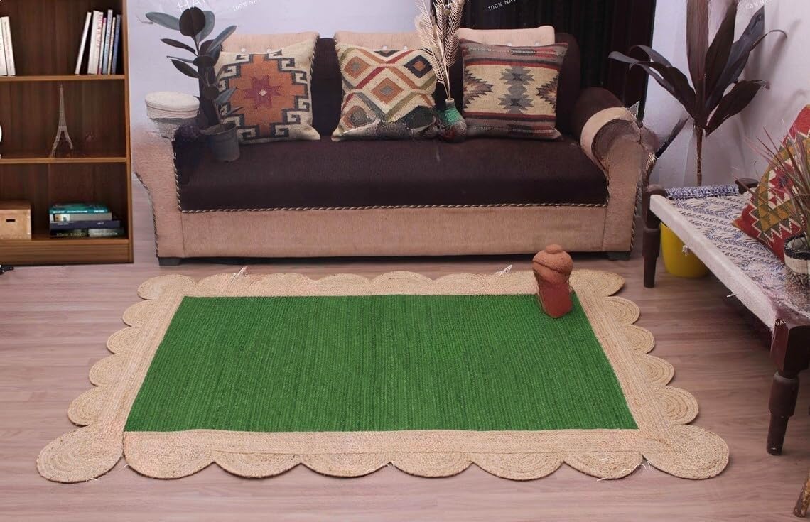 A rectangular green woven rug with a scalloped natural jute border, styled on a wooden floor in a living room setting in front of a sofa.