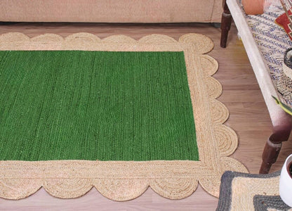 A rectangular green woven rug with a scalloped natural jute border, shown on a light wood floor in a home setting.