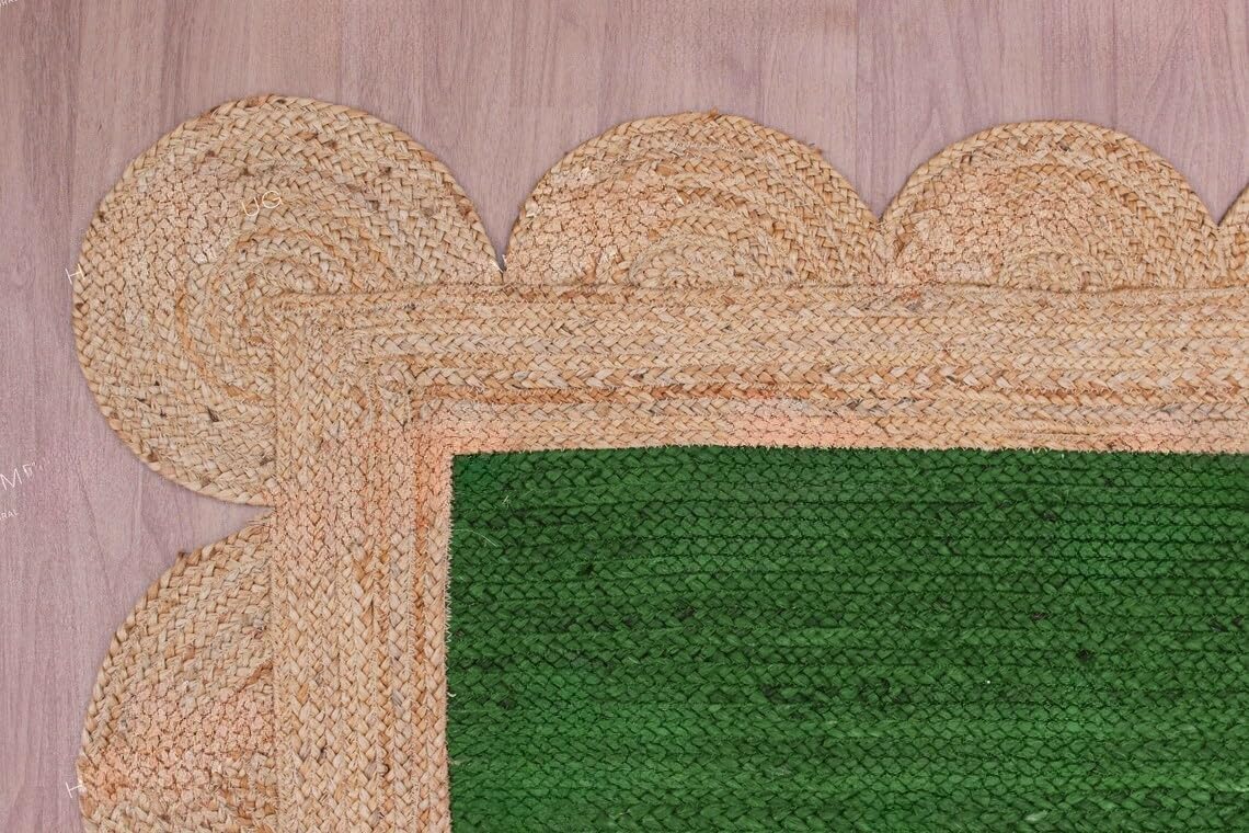 A close-up of a woven rug corner showing a natural tan jute border with scalloped edges and a vibrant green textured center, laid on a light wood floor.