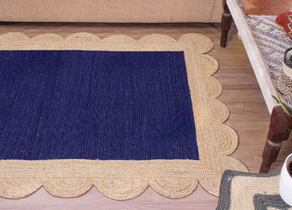 A rectangular woven rug with a deep navy blue center and a natural beige braided border, styled on a light wood floor in a home setting.