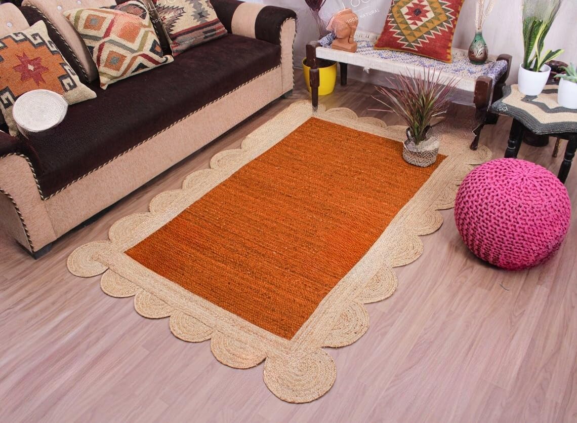 A rectangular woven rug with a warm orange center and a natural beige scalloped border, displayed on a light wood floor in a styled living room setting.